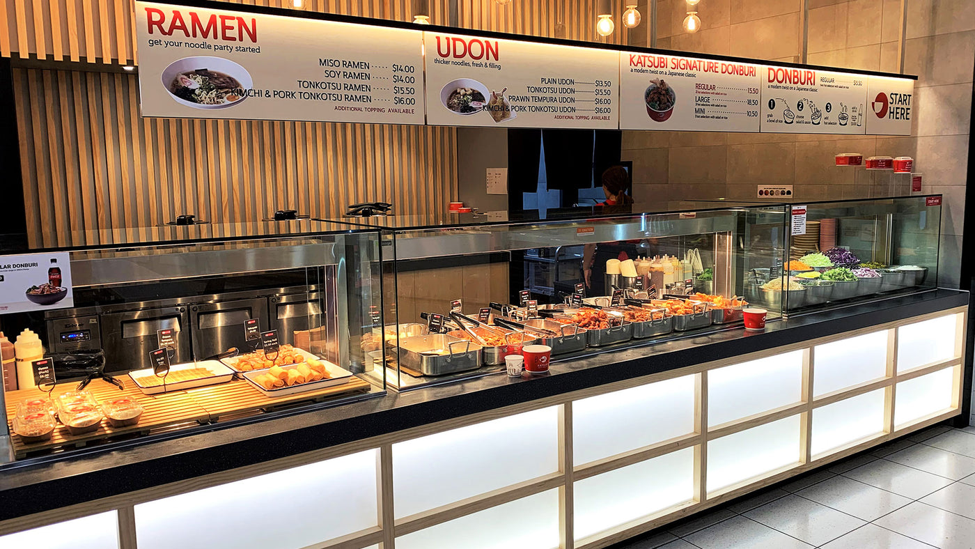 Bakery counter with various food items and a signboard displaying menu options.